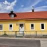 Hausansicht, © Christoph Menhofer Gelbes Haus mit rotem Dach und mehreren Fenstern, umgeben von einem grünen Zaun.