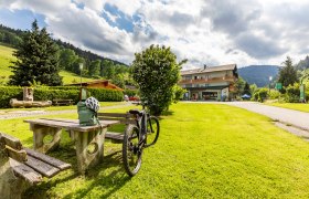 Hubertushof, © Wiener Alpen/Martin Fülöp Ein Fahrrad steht neben einem Picknicktisch auf einer grünen Wiese vor einem Gebäude namens Hubertushof.