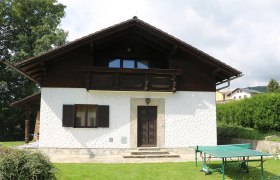 Hauseingang, © Pamela Hniliczka Ein weißes Haus mit Holzbalkon und Tischtennisplatte im Garten.