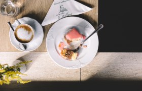 Punschkrapferl und hausgemachte Torten, © Niederösterreich Werbung/Mara Hohla Ein Teller mit einem halben Punschkrapferl und eine Tasse Kaffee auf einem Tisch.