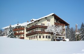 Ramswirt im Winter, © Ramswirt, Familie Pichler Ein großes, traditionelles Gebäude im Schnee mit Holzverzierungen und einem verschneiten Baum im Vordergrund.
