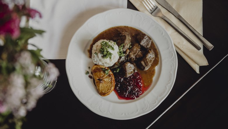 Wirtshausklassiker: Hirschragout, Knödel, Preiselbeeren, © Niederösterreich-Werbung/Sophie Menegaldo Ein Teller mit Hirschragout, Knödel, Preiselbeeren und einer gebratenen Zitronenscheibe.