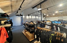 Shop in der Wexl Base, © Wexl Arena St. Corona am Wechsel Innenansicht eines Sportgeschäfts mit Holzdecke und Kleidung auf Kleiderständern.