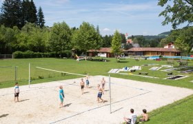 Freibad Aspang, © Freibad Aspang Kinder spielen Volleyball auf einem Sandplatz im Freibad Aspang, umgeben von grüner Wiese und Bäumen.