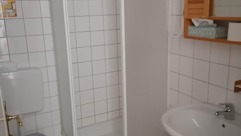 Badezimmer, © Karl Buchner Ein kleines, weiß gefliestes Badezimmer mit Dusche, Toilette und Waschbecken.