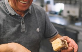Versteht sein Handwerk: Johann Kernbeis, © Niederösterreich Werbung/Mara Hohla Ein älterer Mann in einer Küche hält ein Stück Kuchen und lächelt.