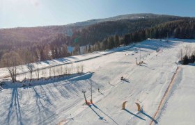 Familienskiland der Wexl Arena St. Corona am Wechsel, © Wexl Arena St. Corona am Wechsel Luftaufnahme eines verschneiten Skigebiets mit Pisten und Wald im Hintergrund.