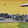 Terrasse, © Christoph Menhofer Terrasse mit gelber Hauswand, grauen Sitzmöbeln, Esstisch, Stühlen und Sonnenschirm.