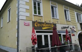 Overland, © Wiener Alpen Gelbes Gebäude mit dem Schriftzug 'Overland' und roten Sonnenschirmen.