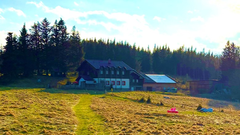 Kampsteiner Schwaig, © Kampsteiner Schwaig Ein Bauernhaus auf einer Wiese, umgeben von Bäumen und unter einem blauen Himmel.