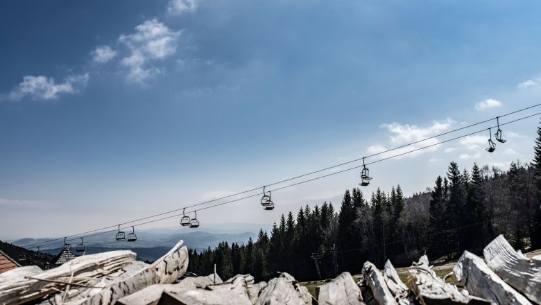 Alpengasthof Enzian, © Alpengasthof Enzian/Thomas Gobauer Blick auf eine Seilbahn über einem Wald mit blauem Himmel im Hintergrund.