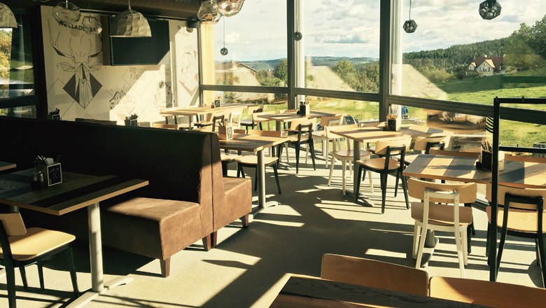 Rasten & Genießen mit Ausblick in der Wexl Lounge, © Wexl Arena St. Corona am Wechsel Innenansicht der Wexl Lounge mit Tischen und Stühlen, große Fenster mit Blick auf die Landschaft.