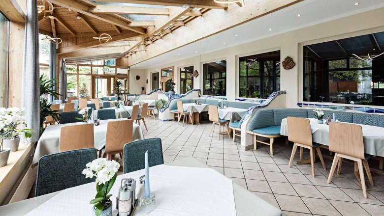 Wintergarten, © Molzbachhof Ein heller Wintergarten mit gedeckten Tischen und Holzmöbeln.