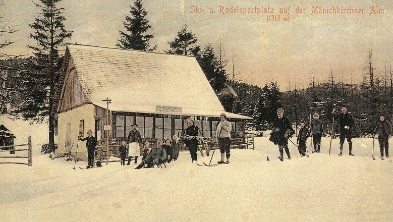 Wintersportort mit Geschichte, © Berggasthof Mönichkirchner Schwaig Historische Postkarte eines Skigebiets mit Menschen auf Skiern vor einer Hütte im Schnee.