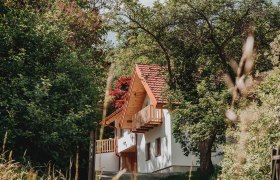 Yogahof, © Sabrina Stummer Ein weißes Haus mit rotem Ziegeldach, umgeben von Bäumen und Pflanzen.