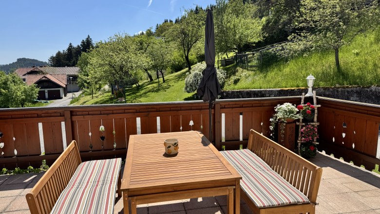 Ferienwohnung Koglhof, © Andrea Tauchner/Koglhof Terrasse mit Holzmöbeln und Blick auf grüne Wiesen und Bäume.