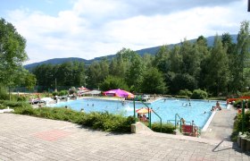 Freibad Kirchberg am Wechsel, © Steindy, CC BY-SA 2.0 DE Freibad mit Schwimmern und Sonnenschirmen, umgeben von Bäumen und Hügeln.
