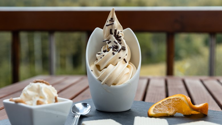 Kulinaria, © MAXSAM GmbH_perfect print Ein Dessert mit Softeis, Schokostreuseln, Waffeln und Orangenscheibe auf einem Tisch.