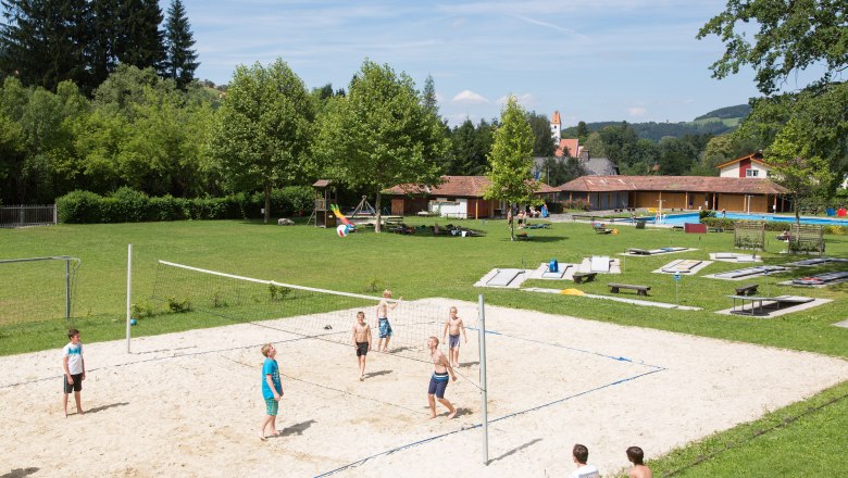 Freibad Aspang, © Freibad Aspang Kinder spielen Volleyball auf einem Sandplatz im Freibad Aspang, umgeben von grüner Wiese und Bäumen.