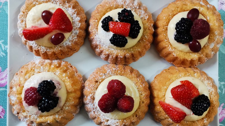 Saisonale und hausgemachte Leckerein, © Wiener Alpen Sechs kleine Obsttörtchen auf einem weißen Teller, dekoriert mit Beeren und Sahne.