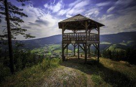 Kernstockwarte Kirchberg am Wechsel, © Wiener Alpen, Foto: Christian Kremsl Holzaussichtsturm mit Blick auf grüne Täler und Berge unter blauem Himmel.
