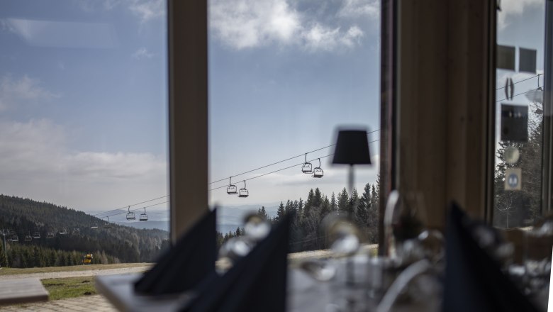 Alpengasthof Enzian, © Alpengasthof Enzian/Thomas Gobauer Blick aus einem Fenster auf eine Berglandschaft mit Sessellift und Wald.