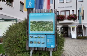 Wanderstartplatz, © Wiener Alpen Wanderkarte vor dem Gemeindeamt Kirchberg am Wechsel mit Hinweisschildern und Flaggen.
