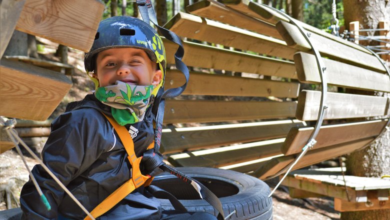 Kinderparcours, © Hamari Kletterpark Ein Kind mit Helm und Sicherheitsgurt in einem Kletterpark.
