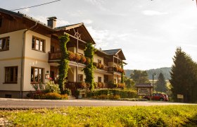 Herzlich Willkommen, © Ofnerhof Ein traditionelles Gasthaus mit Blumen geschmückten Balkonen in ländlicher Umgebung bei Sonnenuntergang.