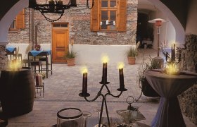 Café Fenz mit gemütlichem Schanigarten und neu gestaltetem Innenhof, © Café Fenz Gemütlicher Innenhof eines Cafés mit Kerzenlicht und rustikaler Steinmauer.