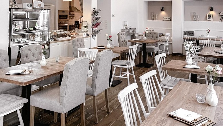 Mille Fleurs Café & More, © Gemeinde Aspang, Mille fleur Innenansicht eines gemütlichen Cafés mit Holztischen und gepolsterten Stühlen.