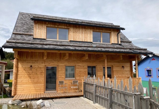 Holzchalet mit zwei Ferienwohnungen und Terrasse, umgeben von einem Holzzaun.