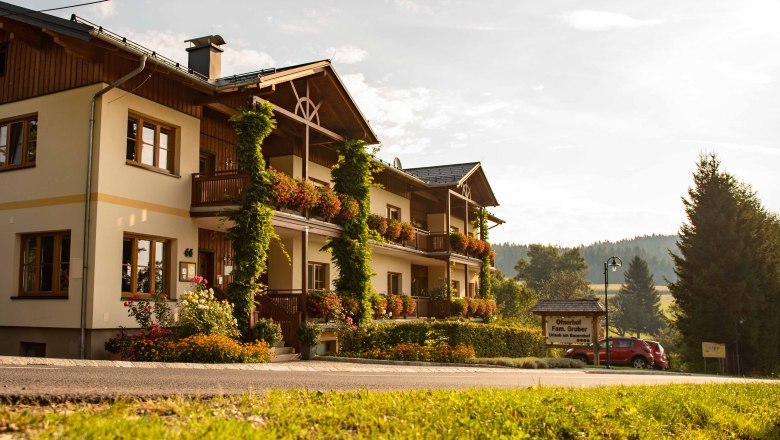 Ein traditionelles Gasthaus mit Blumen geschm&uuml;ckten Balkonen in l&auml;ndlicher Umgebung bei Sonnenuntergang.