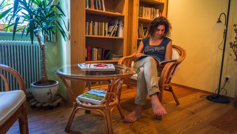 Frau liest in einem gem&uuml;tlichen Leseraum mit B&uuml;cherregal und Pflanzen.