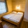 Gemütliches Schlafzimmer mit Holzwänden, Doppelbett und Fenster mit Vorhängen.