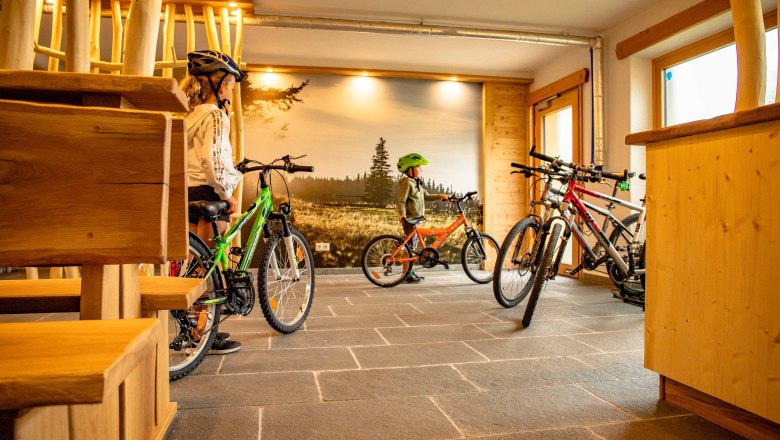 Kinder mit Fahrr&auml;dern in einem Raum mit Holzm&ouml;beln und Landschaftsfototapete.