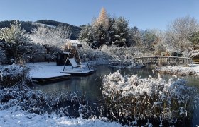 Winterlicher Garten mit Teich, Brücke und Schaukel im Schnee.