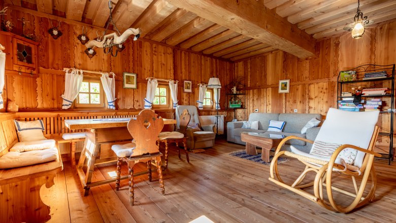 Essbereich mit Holzmöbeln, Schaukelstuhl und Sofa in einem Raum mit Holzvertäfelung.