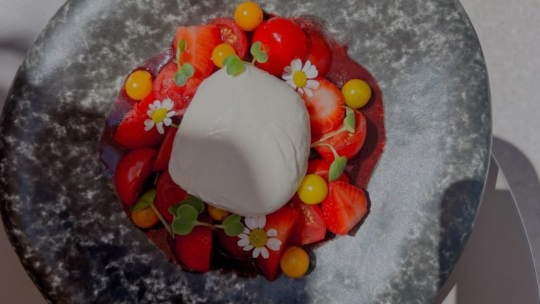 Ein Teller mit Burrata, Erdbeeren, Tomaten und essbaren Blüten.