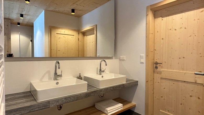 Modernes Badezimmer mit zwei Waschbecken, Holzdecke und -türen.