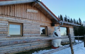 Holzhütte mit Eisbärfigur und Schneeresten im Vordergrund.