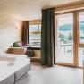 Modernes Hotelzimmer mit Holzwänden, großem Bett und Balkon mit Bergblick.