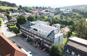 Luftaufnahme eines Hotels mit Solarpanelen auf dem Dach, umgeben von B&auml;umen und weiteren Geb&auml;uden in einer l&auml;ndlichen Gegend.