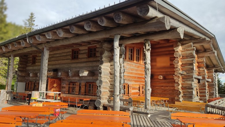 Holzhütte mit Terrasse und Bänken im Freien.