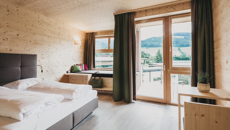 Modernes Hotelzimmer mit Holzw&auml;nden, gro&szlig;em Bett und Balkon mit Bergblick.