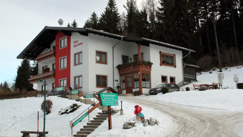 Winterliches Gästehaus Apschner mit Schnee und Wald im Hintergrund.