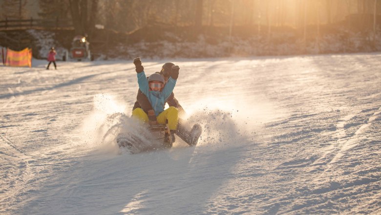 Zwei Personen rodeln im Schnee bei Sonnenuntergang.