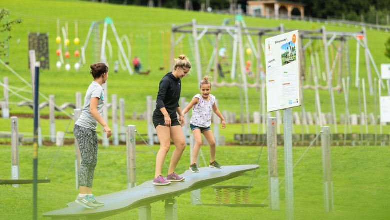Drei Personen balancieren auf einer Wippe im Motorikpark St. Corona.