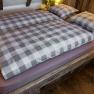 Gemütliches Bett mit kariertem Bettzeug in einer Holzhütte.