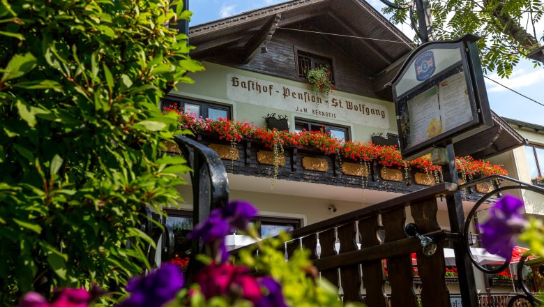 Gasthof Pension St. Wolfgang mit Blumen geschmücktem Balkon und Schild im Vordergrund.